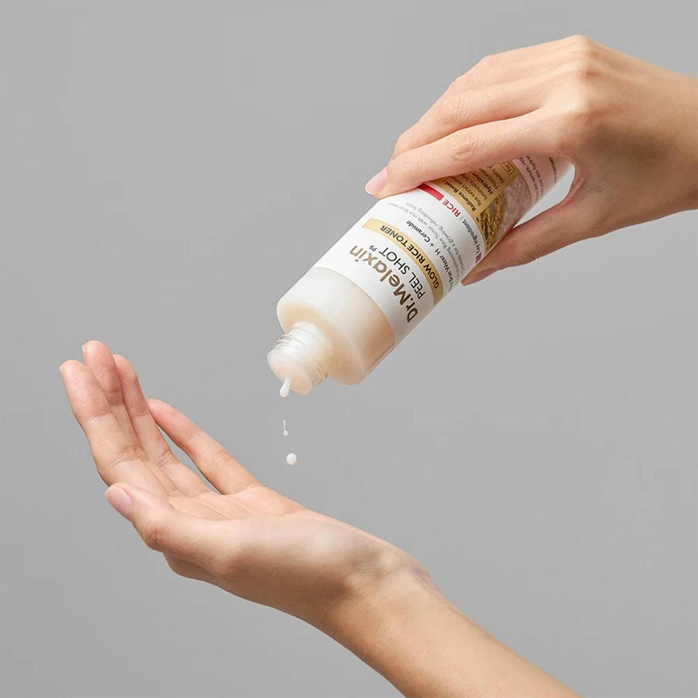 Ένα χέρι κρατάει το μπουκάλι Dr. Melaxin Peel Shot Glow White Rice Toner και στάζει προϊόν στο άλλο χέρι.